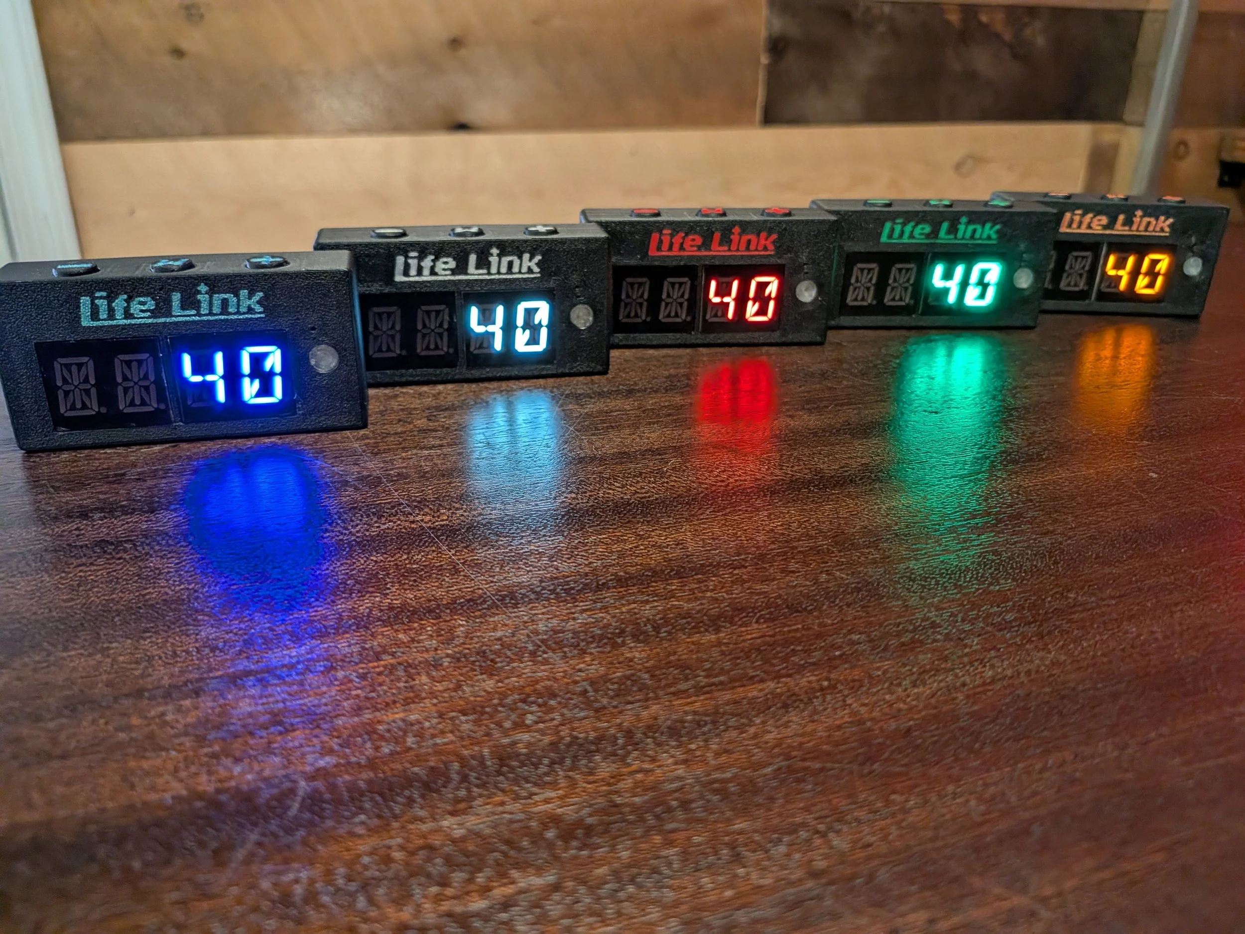 Four digital scoreboards on a wooden surface, displaying scores 40, 40, 40, and 47 in blue, white, red, and orange lights respectively.