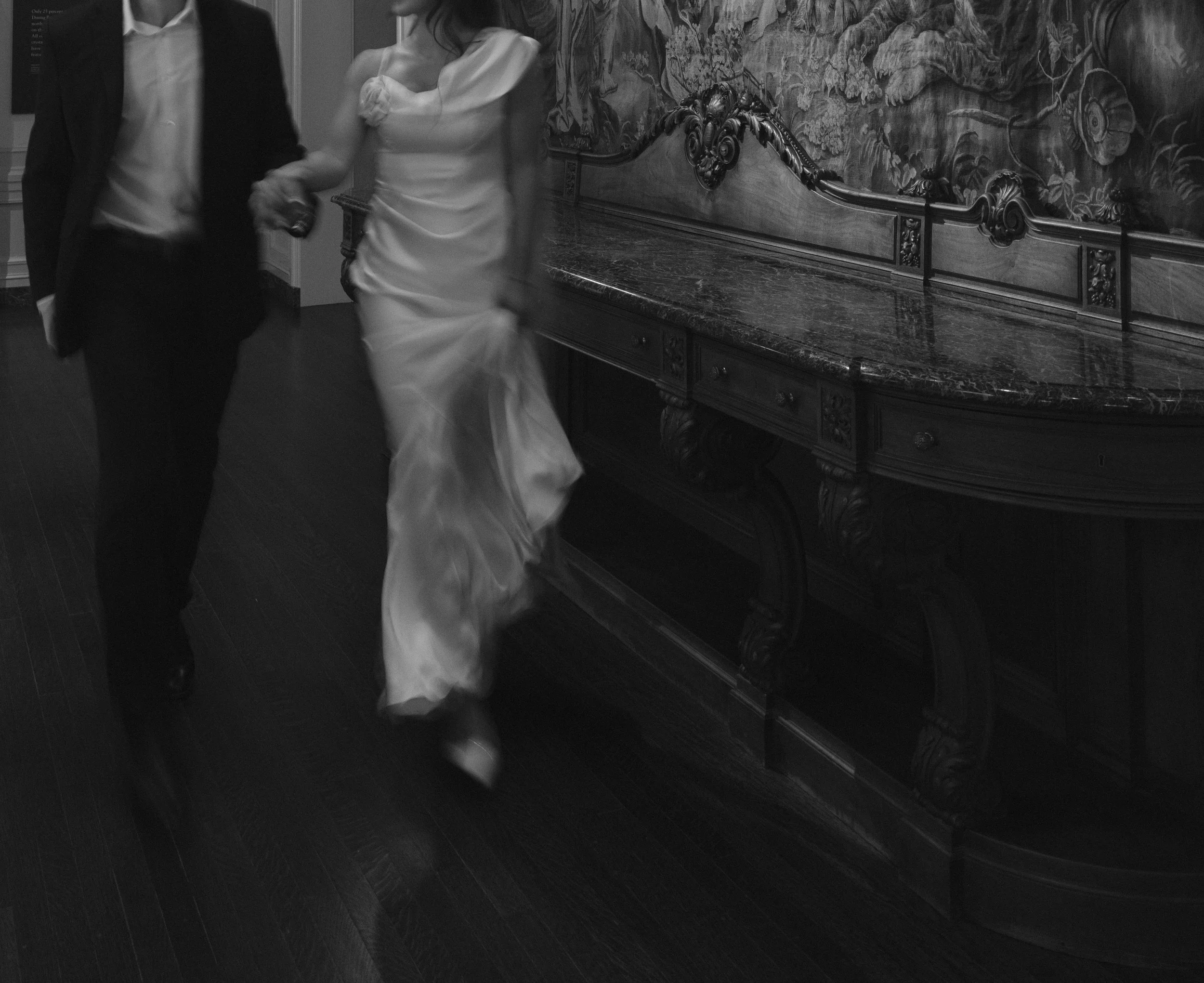 Couple holding hands running through museum in white dress and suit