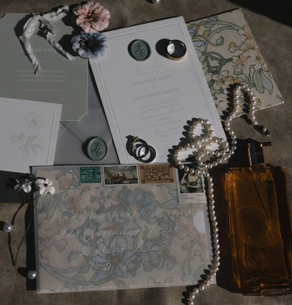 A collection of wedding or formal event items including invitation cards, a pearl necklace, rings, stamps, and decorative elements on a surface.
