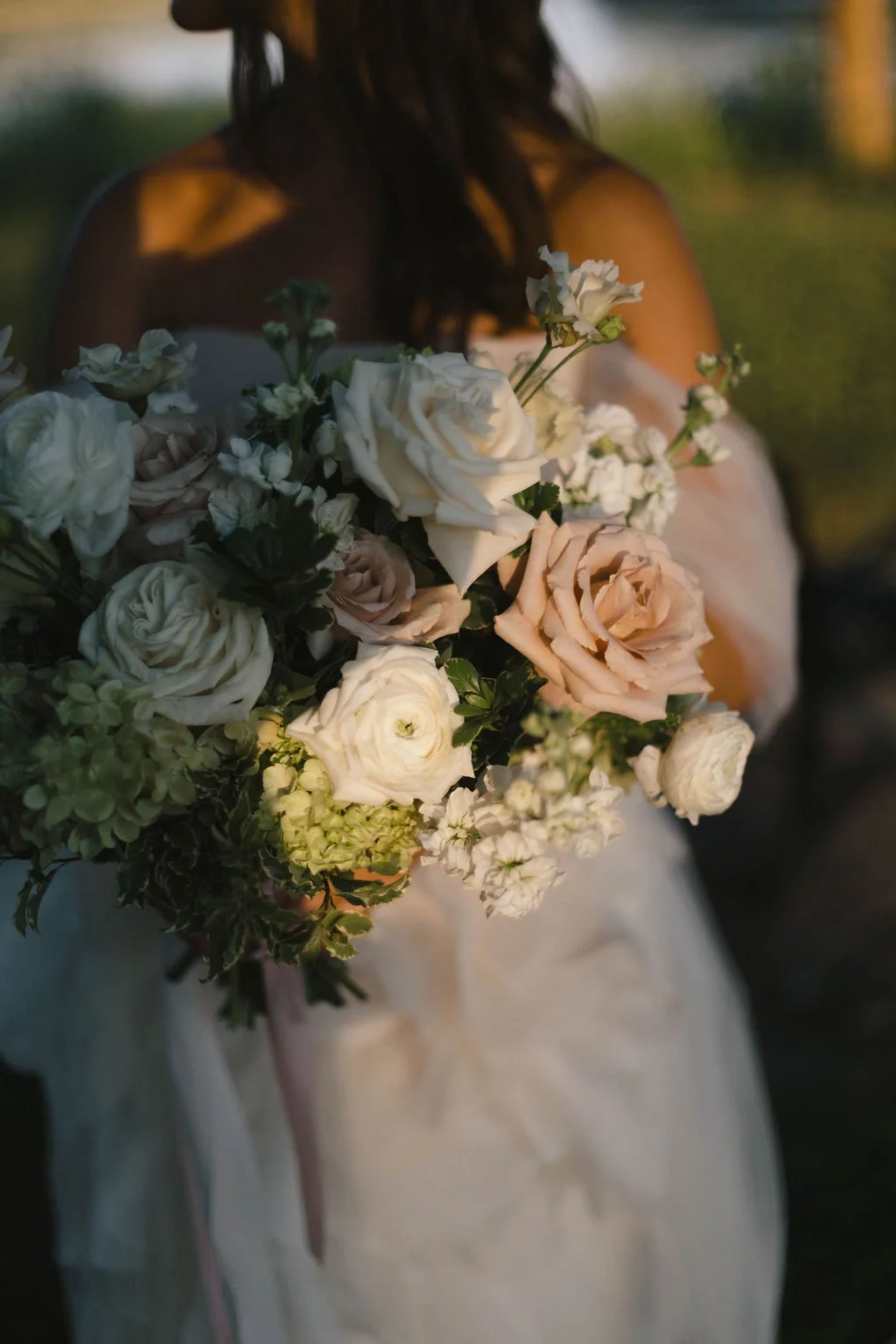 A woman in a white dress holding a large bouquet of white, cream, and pale pink flowers.