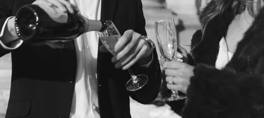 People celebrating with champagne, one person pouring champagne into a glass, others holding glasses, in black and white.