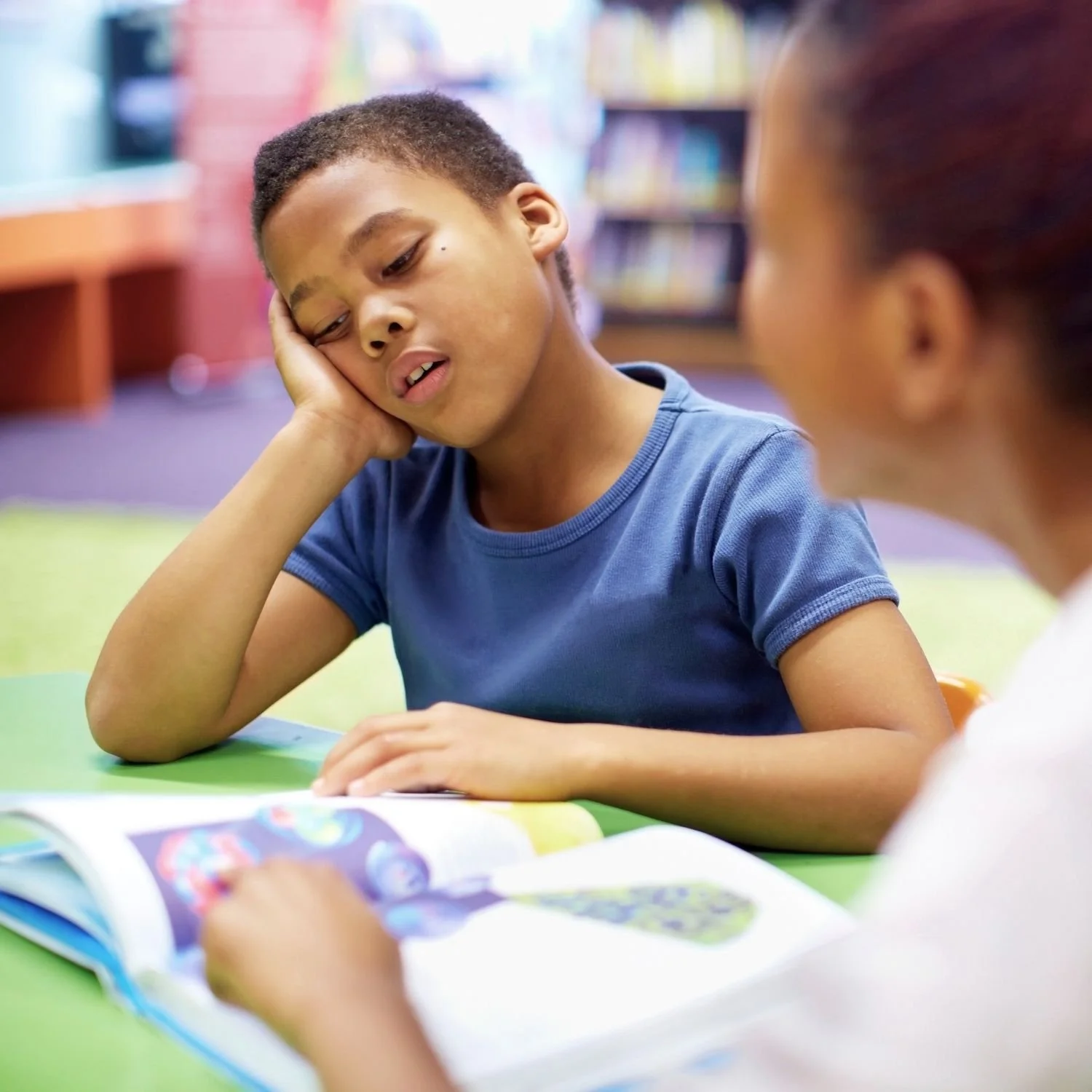 A student rests his head on one hand while reading with an adult.