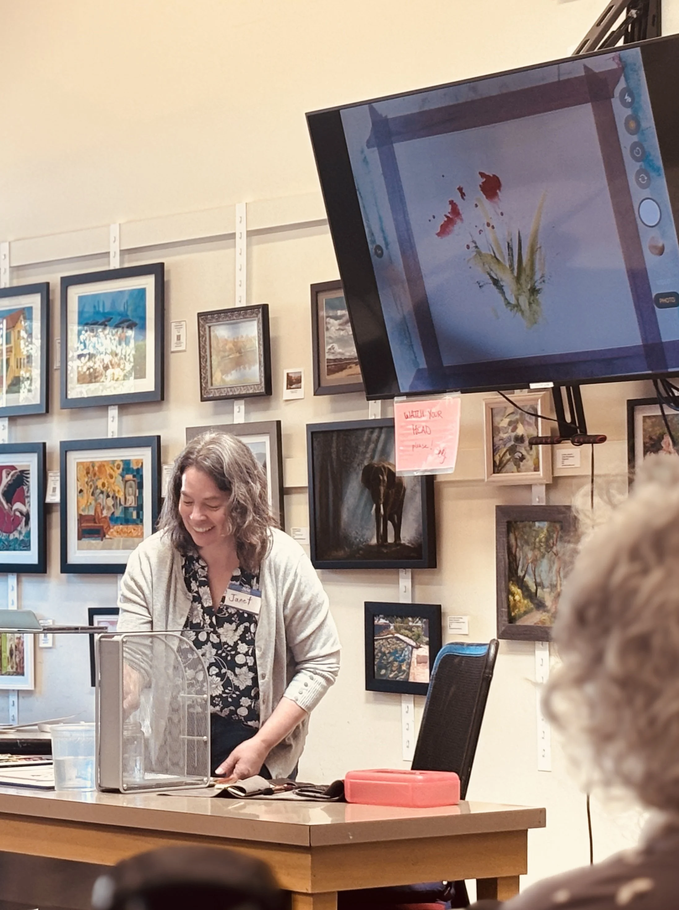 Artist and teacher, Janet Arkills, demonstrates painting loosely with watercolor. Her painting is projected onto a screen behind her so the audience can see every stroke as she paints.