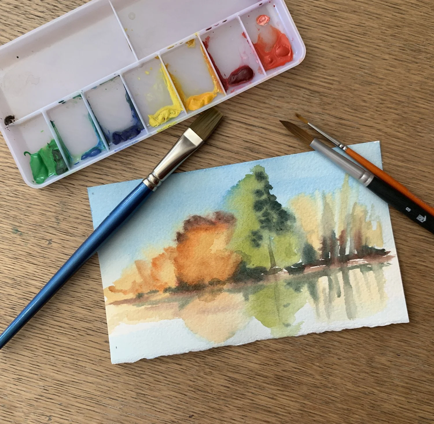 Watercolor palette, brushes and sample watercolor landscape scene