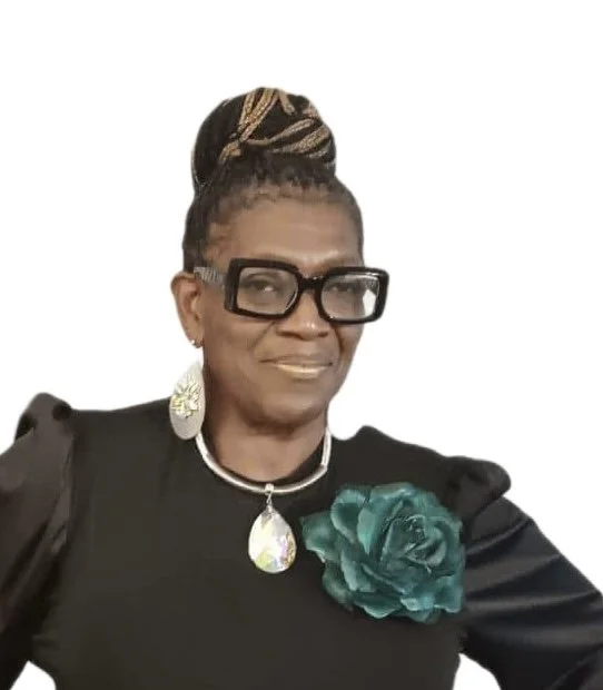 Portrait of a woman wearing glasses, a black dress with a large teal flower, and statement jewelry.
