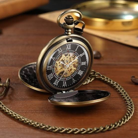 An antique pocket watch with a chain, open to reveal a black dial with Roman numerals and a gold mechanical movement, resting on a wooden surface.