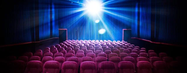Empty theater with pink seats and bright stage lights.