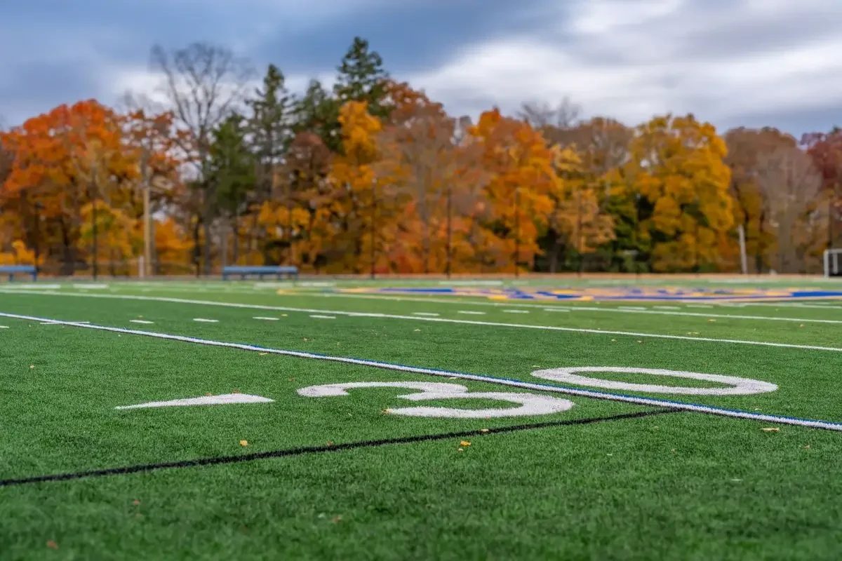 A football field with colorful autumn trees in the background.