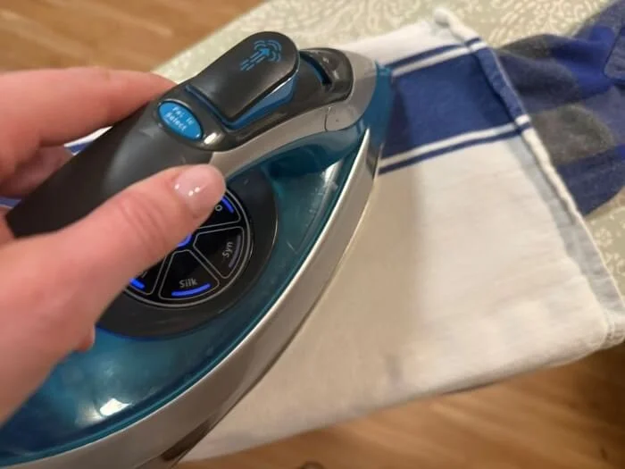 A person ironing a piece of fabric (with elbow patches underneath).