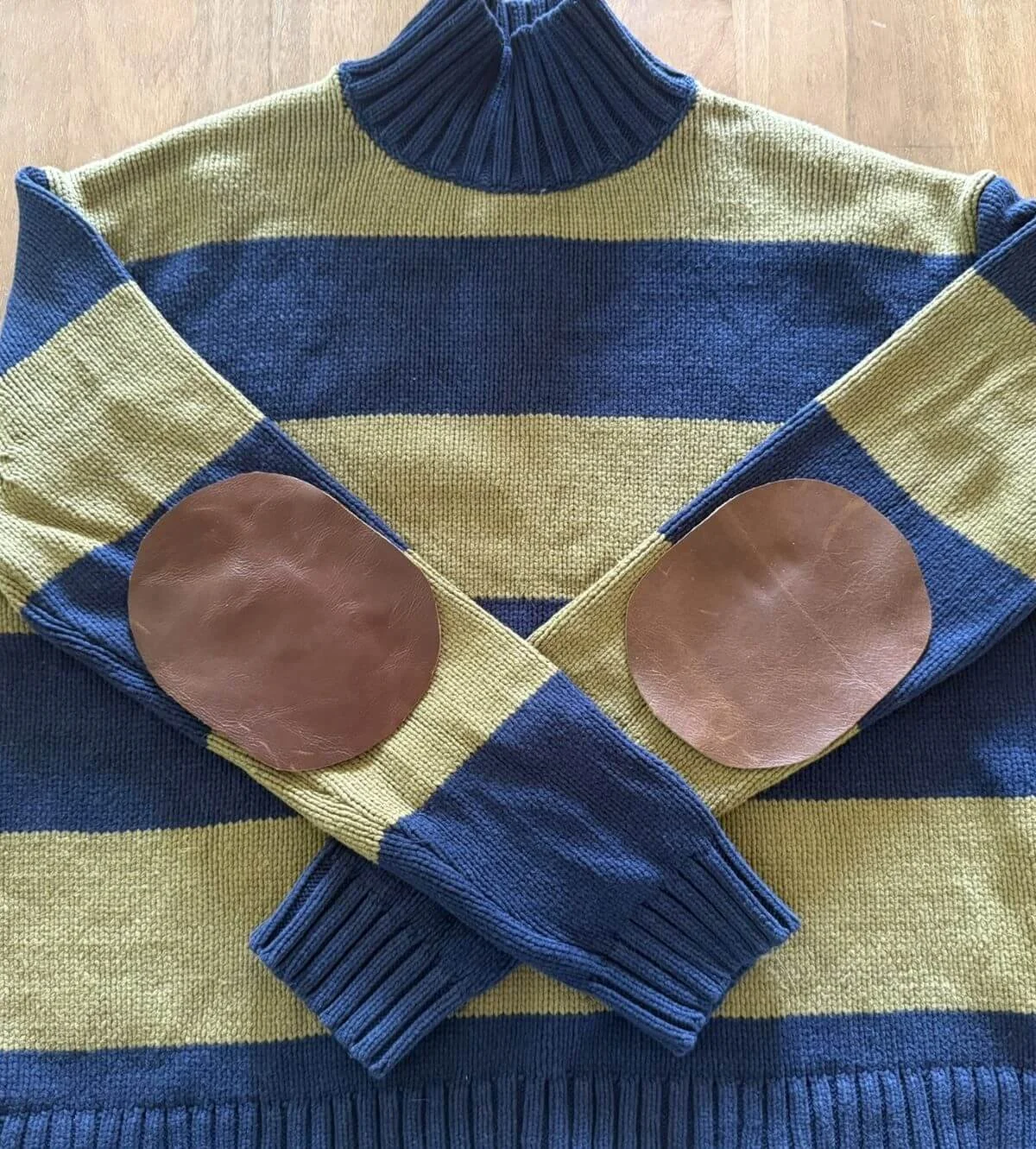 A navy and mustard-colored striped turtleneck sweater with brown leather elbow patches.