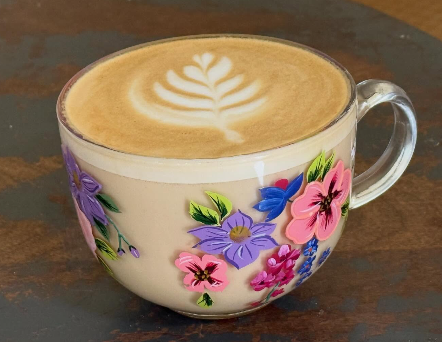 A ceramic mug with a floral pattern filled with coffee featuring latte art in the shape of a fern.