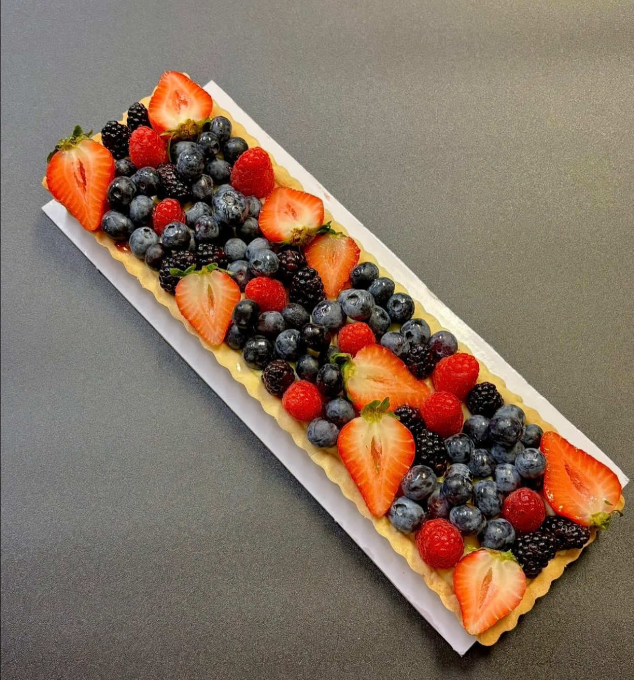 A rectangular fruit tart topped with strawberries, blueberries, raspberries, and blackberries on a gray surface.