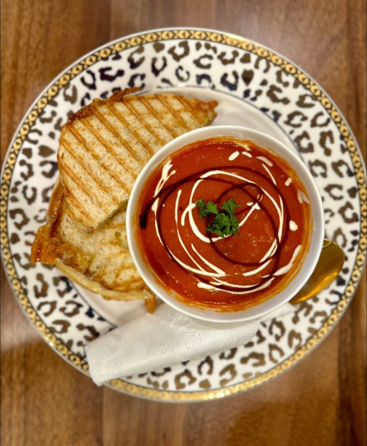 A plate with a grilled sandwich and a bowl of tomato soup garnished with cream and cilantro, on a decorative leopard print plate.