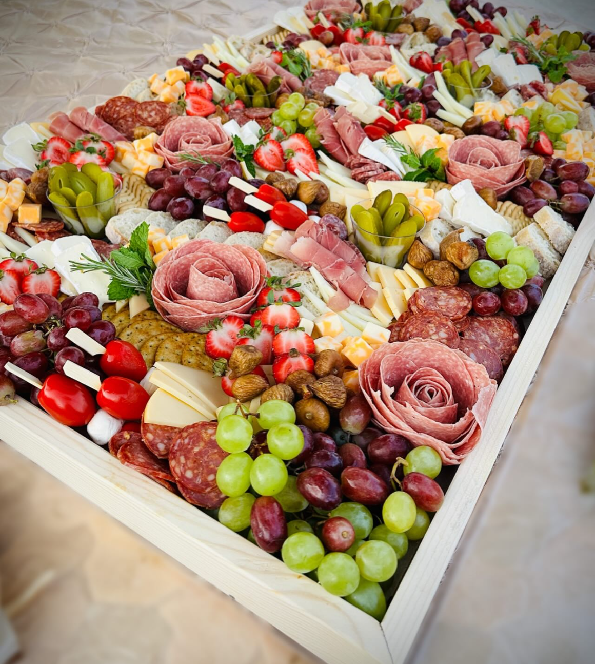 A large wooden tray filled with various types of cured meats, cheeses, grapes, strawberries, and nuts, arranged for a charcuterie snack.