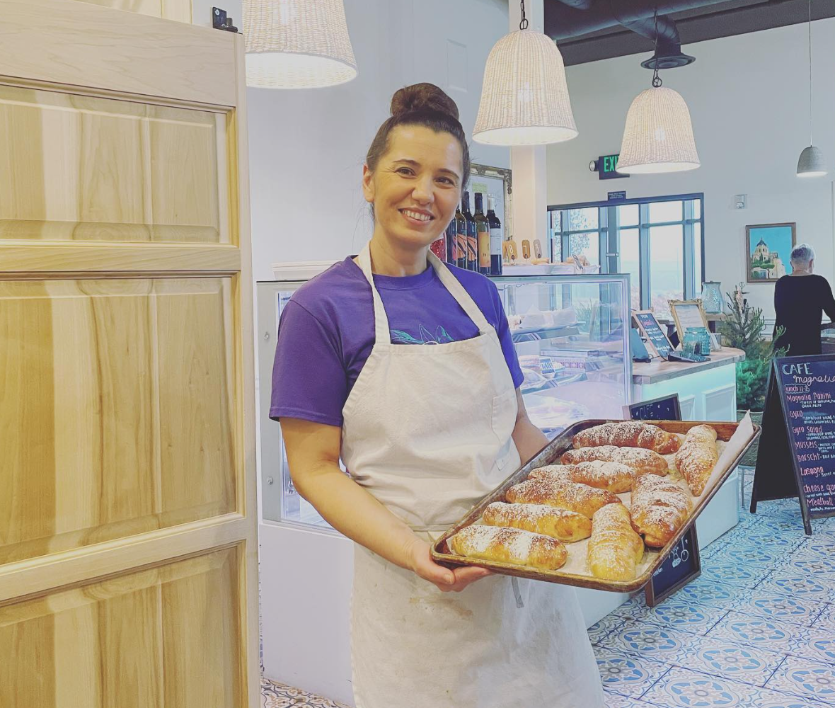 Nena wearing a purple shirt and white apron holding a tray of baked croissants at a Cafe Magnolia.