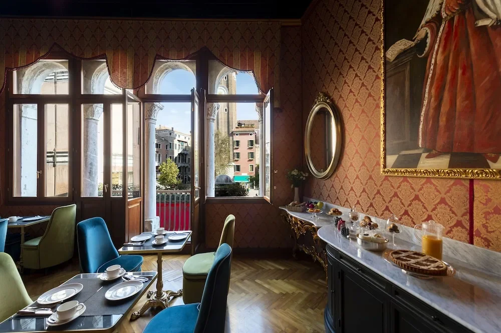 Elegant dining room with colorful chairs, a marble sideboard with breakfast items, and large windows showing a cityscape of European-style buildings.