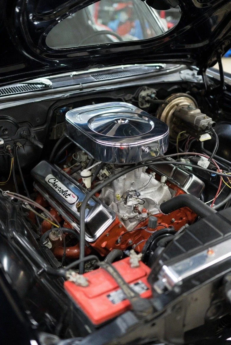 Close-up of a Chevrolet car engine inside the engine bay, featuring chrome and orange components, with a visible Chevrolet logo on the engine valve cover.