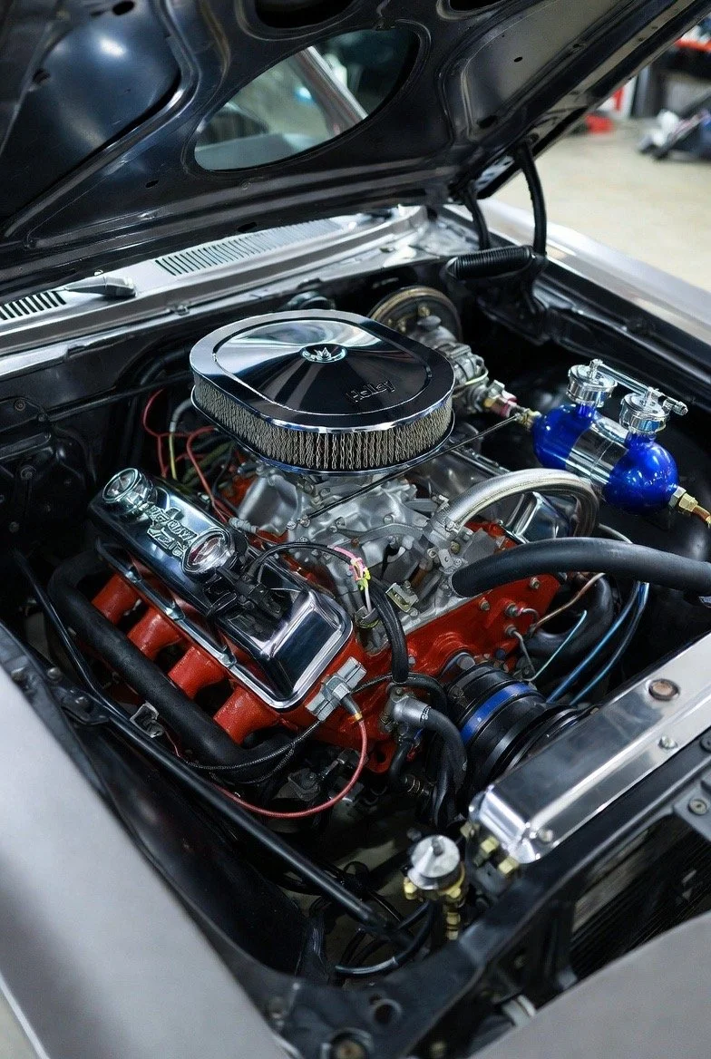 Close-up view of a car engine inside the hood, featuring chrome components, a large air filter, and vibrant blue and orange parts.