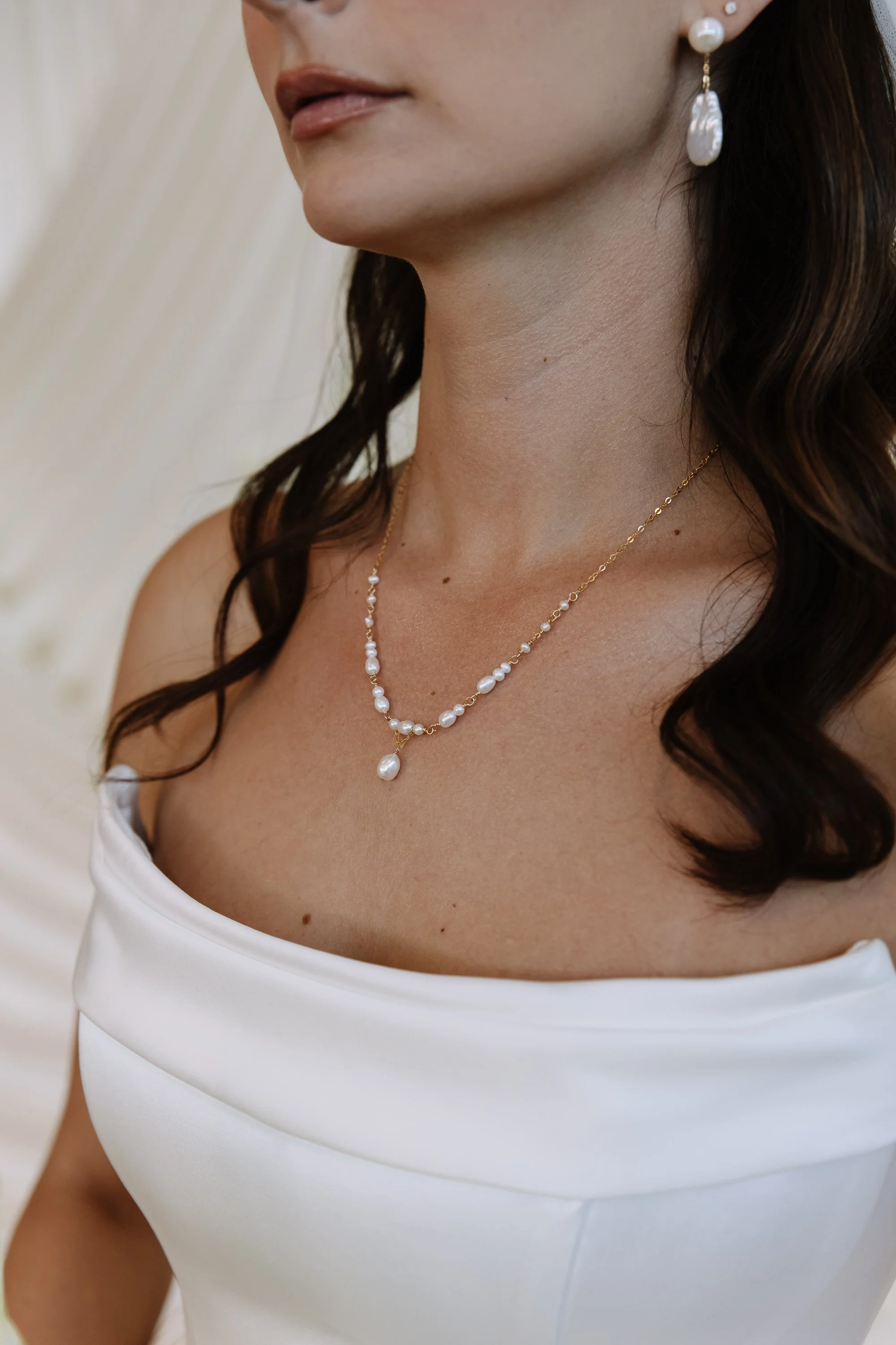 A woman wearing a pearl necklace and earrings, dressed in a white top.