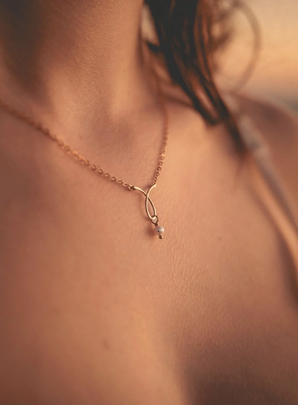 A close-up of a woman's neck and collarbone area wearing a delicate gold necklace with a pearl pendant.