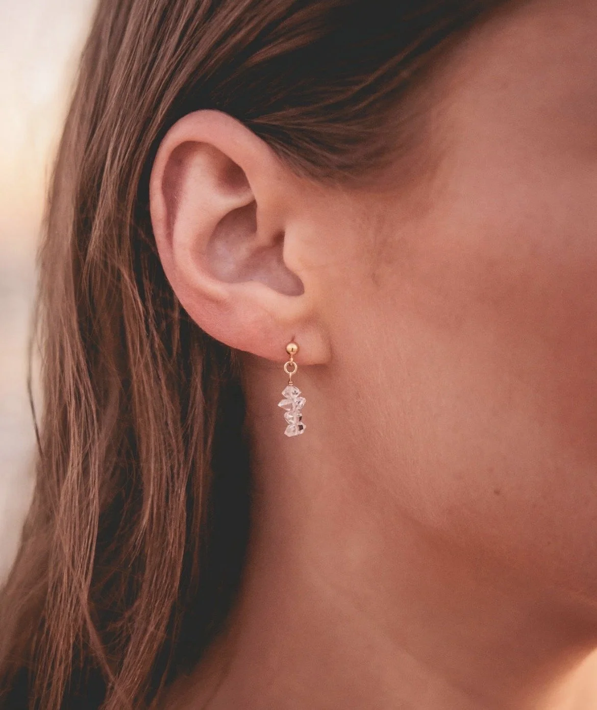 Close-up of a woman's human ear with a gold and crystal earring.