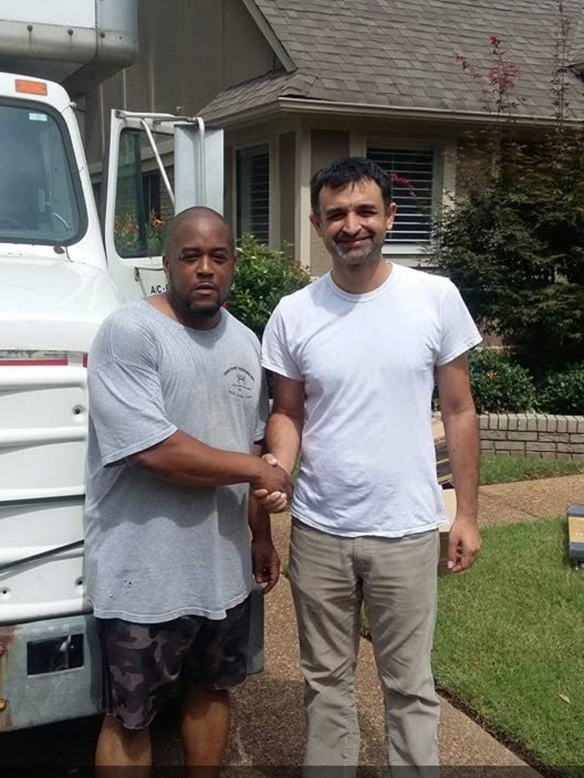 Two men shaking hands in front of a white truck and a house with garden.