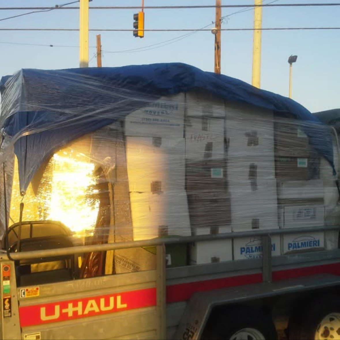 U-Haul truck loaded with boxes covered with a tarp, parked near utility poles and traffic lights at sunset.