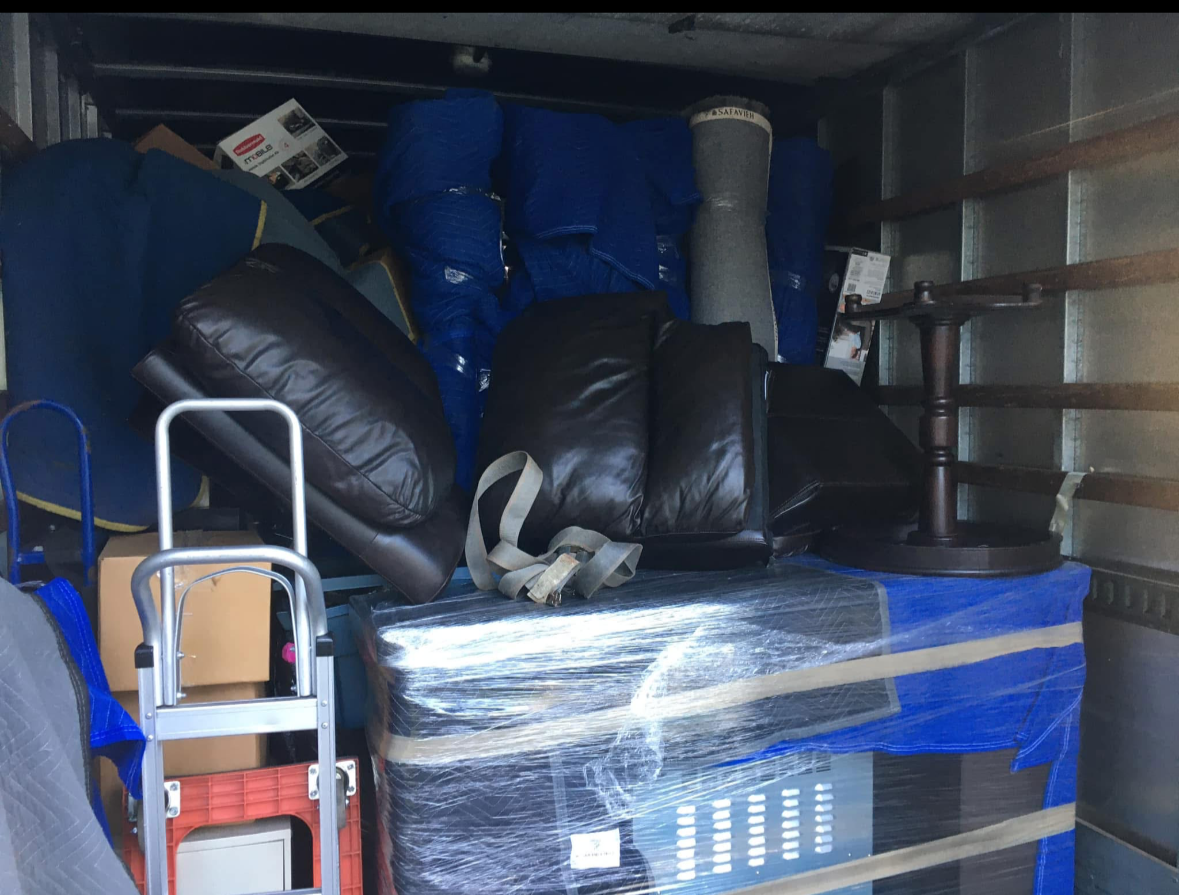 Packed moving truck with furniture, a brown leather chair, a lamp, and boxes wrapped in plastic.
