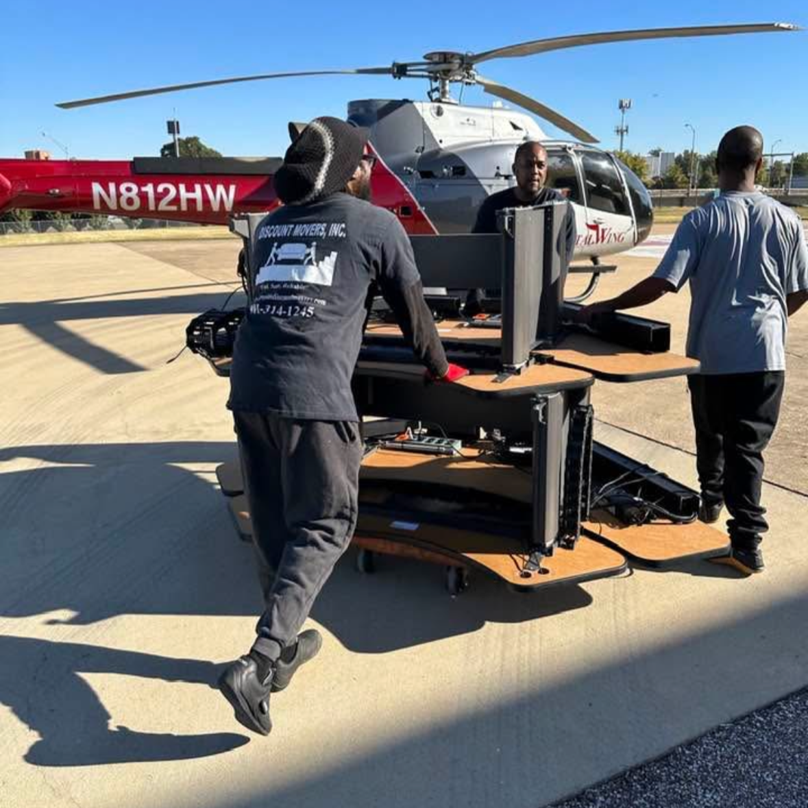 Three men operate a portable computer station outside next to a helicopter on the tarmac.