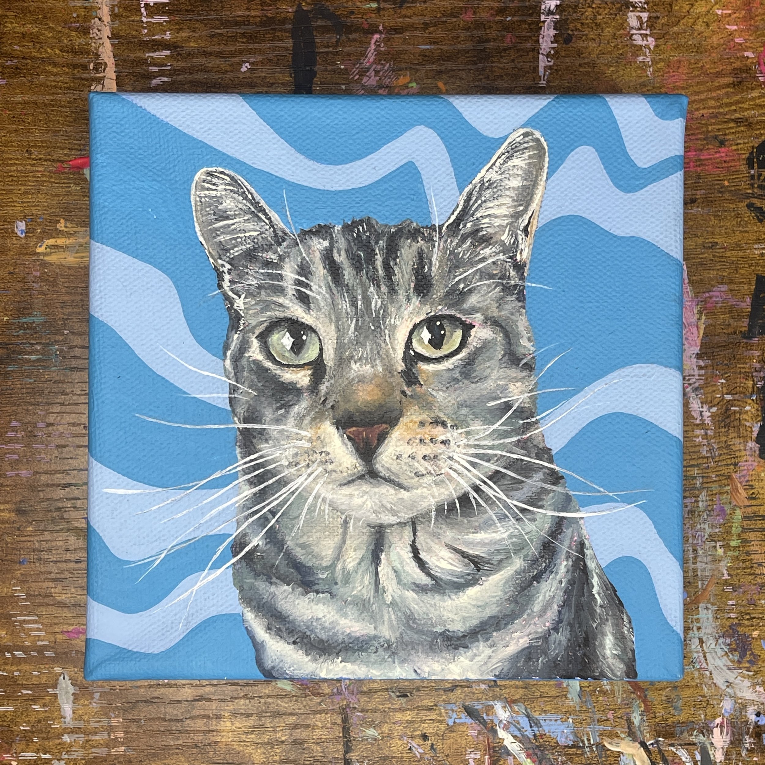 Painting of a kitten against a blue background with white and blue wavy patterns.