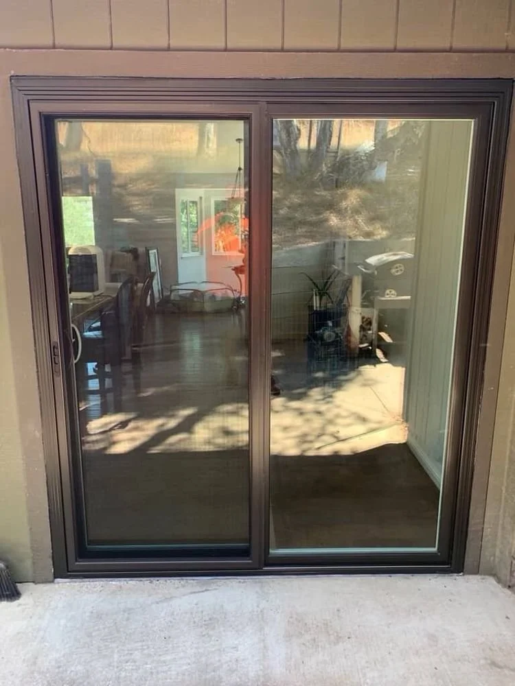 Sliding glass door leading into a dining room with a table, chairs, and a computer setup, and an outdoor area with a potted plant and parked cars.