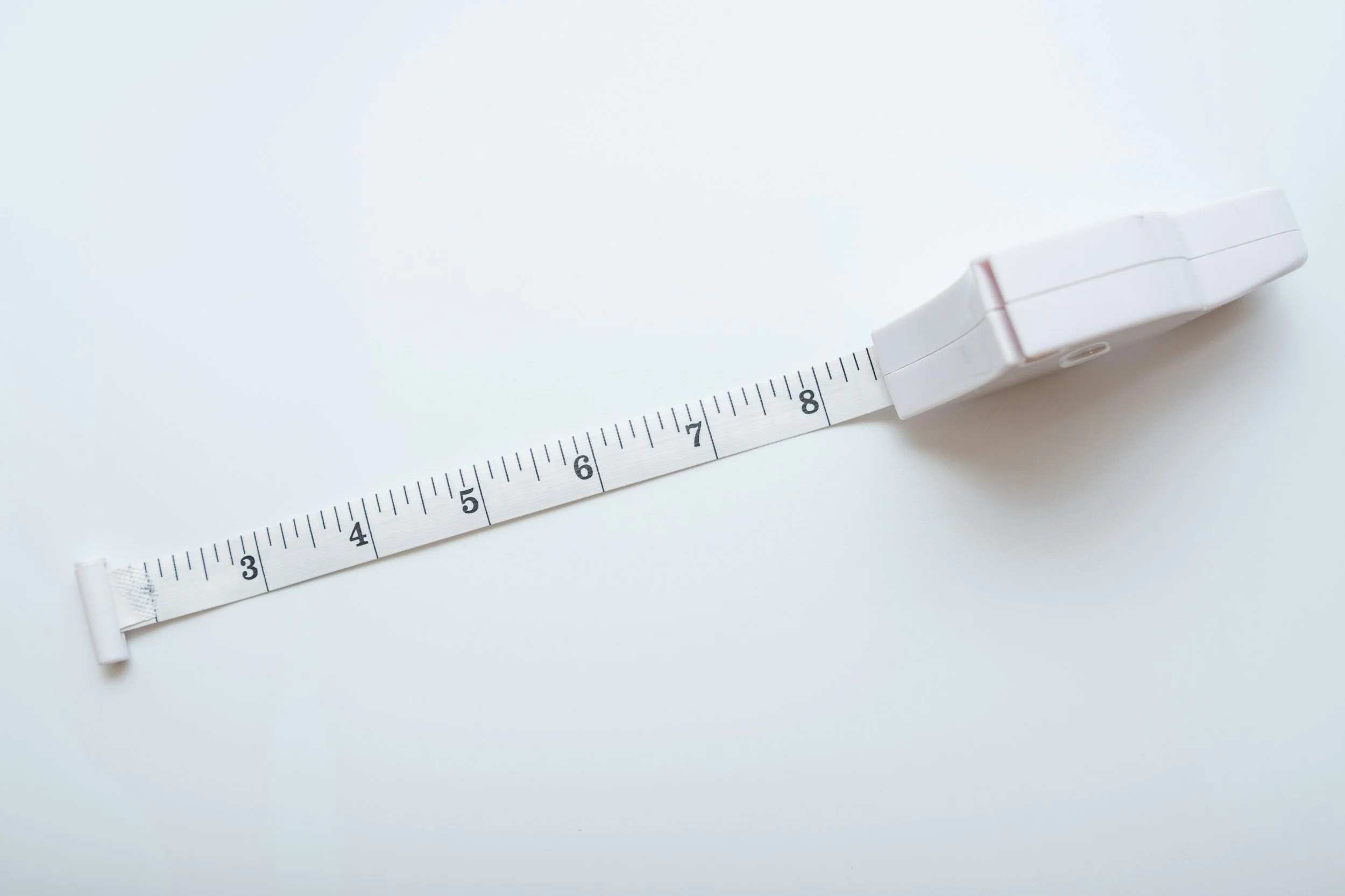 A white measuring tape stretched out on a white surface, with markings indicating inches.