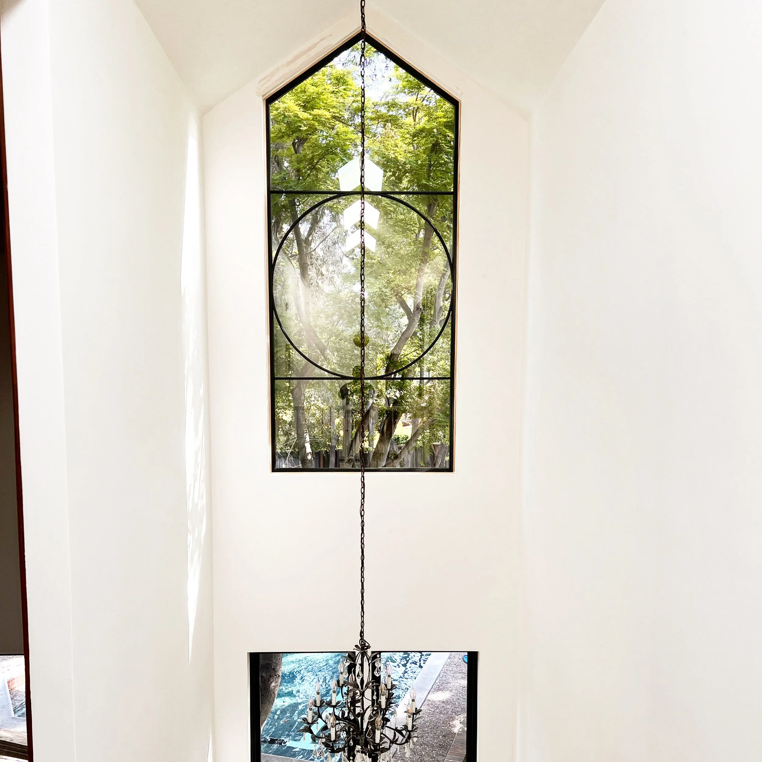 A high ceiling with a large pentagon-shaped window showing green trees outside. A chandelier hangs from the ceiling.