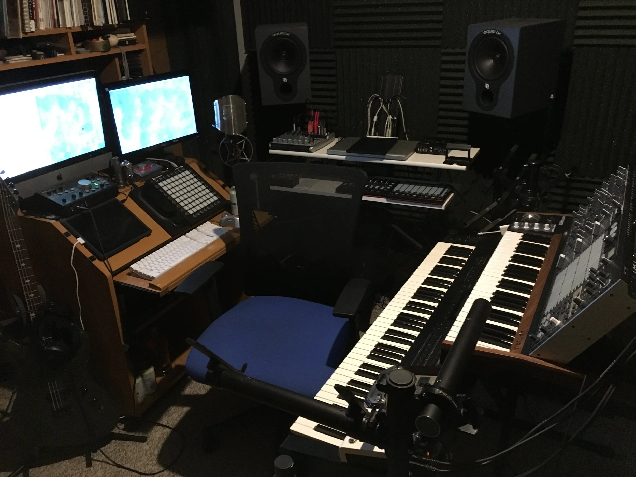 Music production studio with dual monitors, keyboards, audio equipment, studio speakers, and musical instruments.