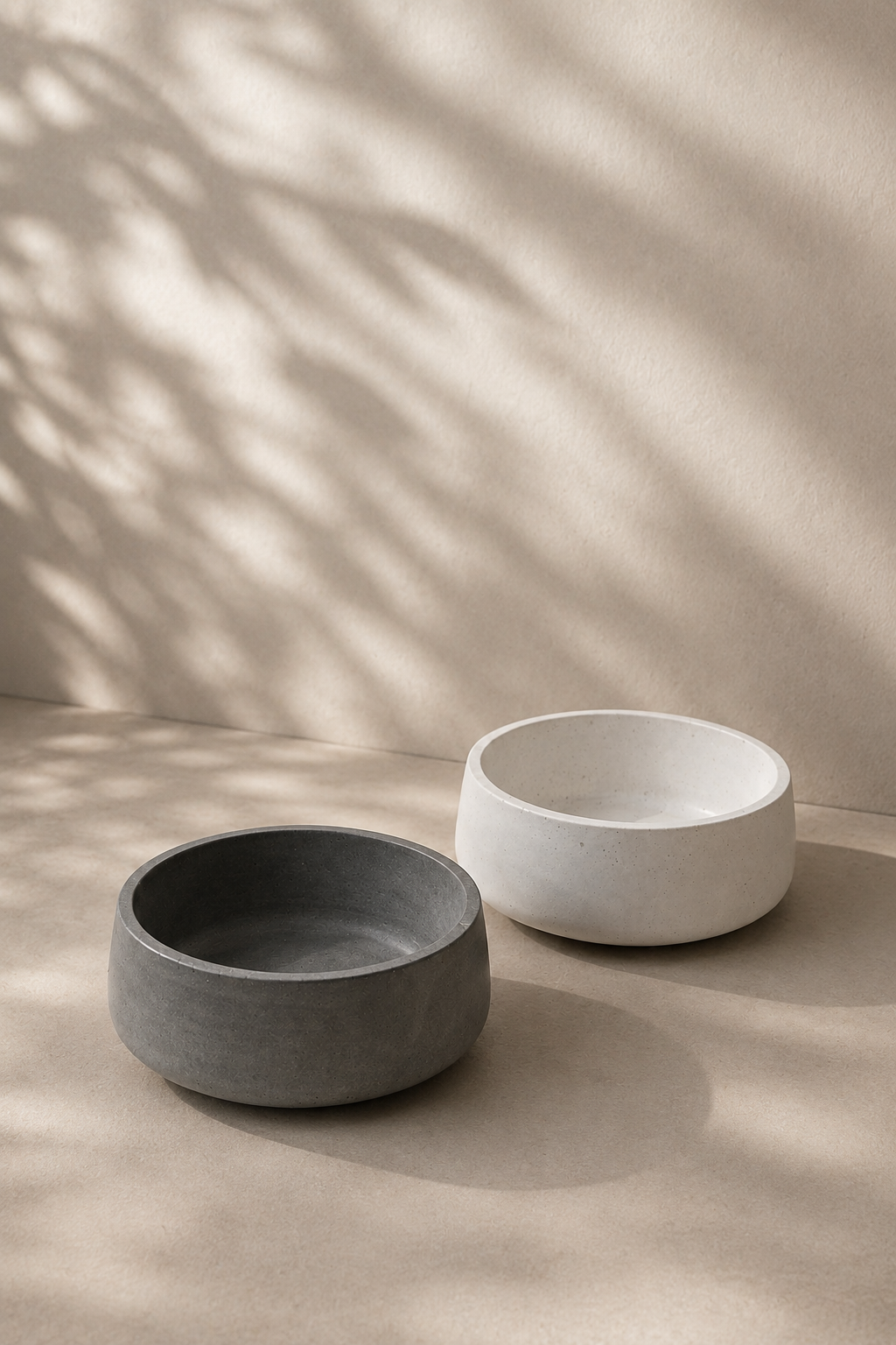 Dois pratos de cerâmica, um preto e um branco, colocados sobre uma superfície de tom claro com sombra de folhas projetada na parede ao fundo.