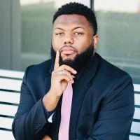 Image of a man in a black suit with a pink tie