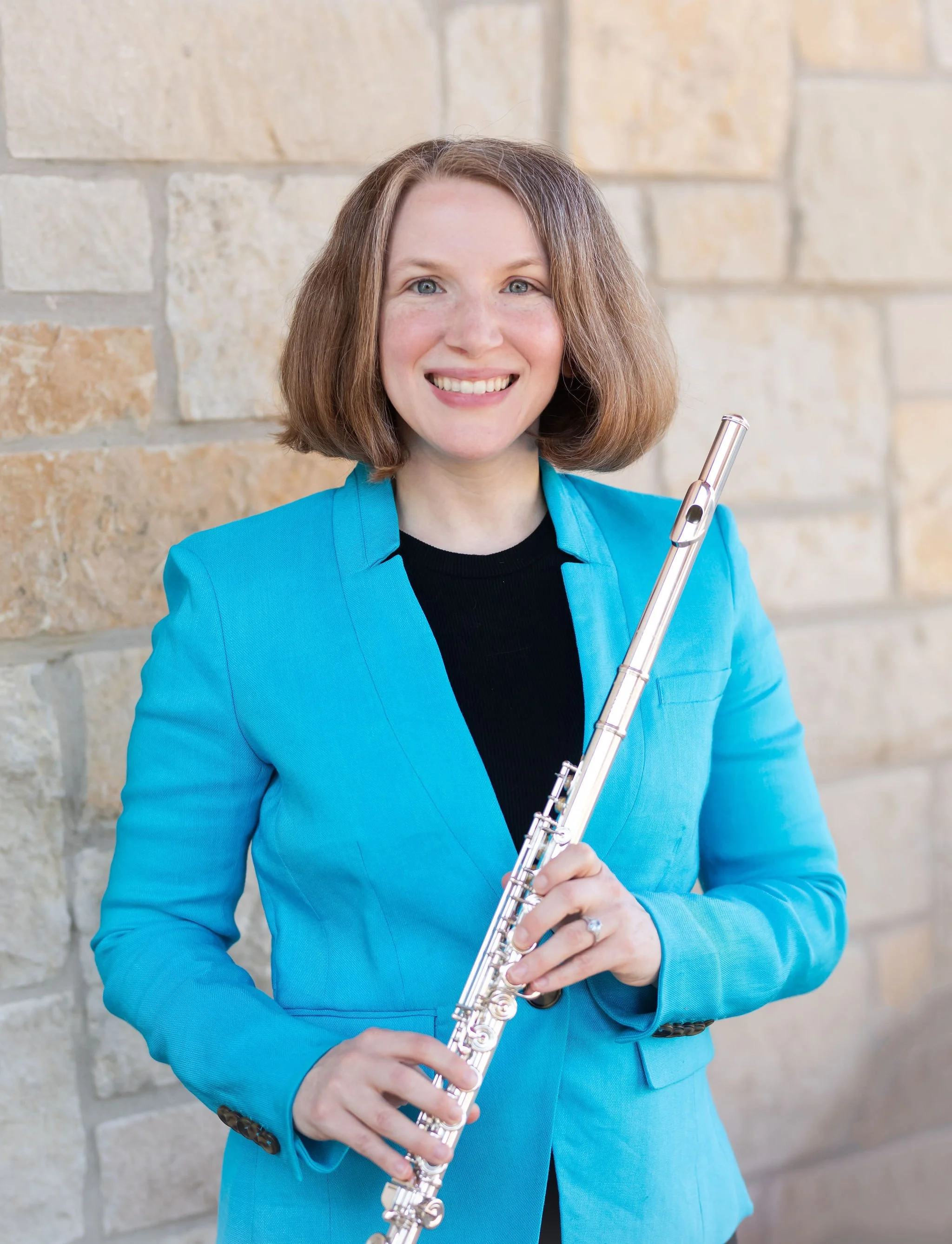A woman wearing a turquoise blazer over a black top holding a silver flute
