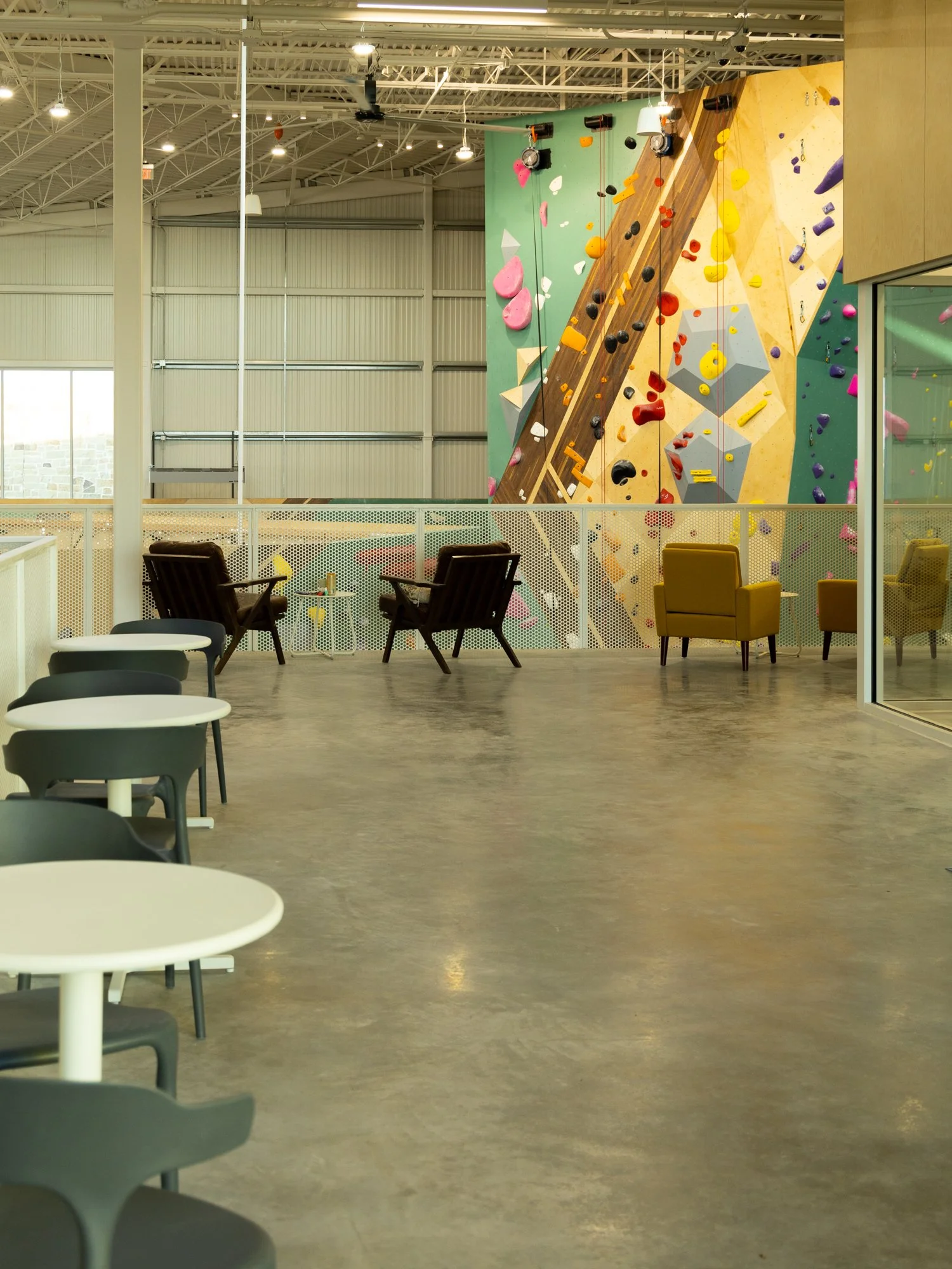 Indoor rock climbing gym with colorful climbing walls and holds, seating area with chairs, tables, and lounge chairs.