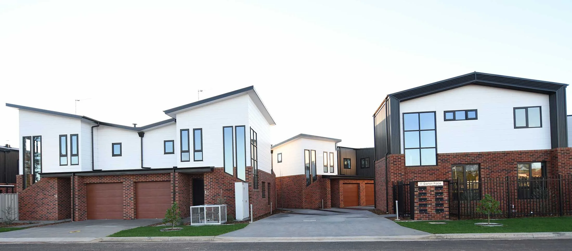 Modern townhouse complex with brick and white siding, black window frames, and multiple levels, located on Garton Place.