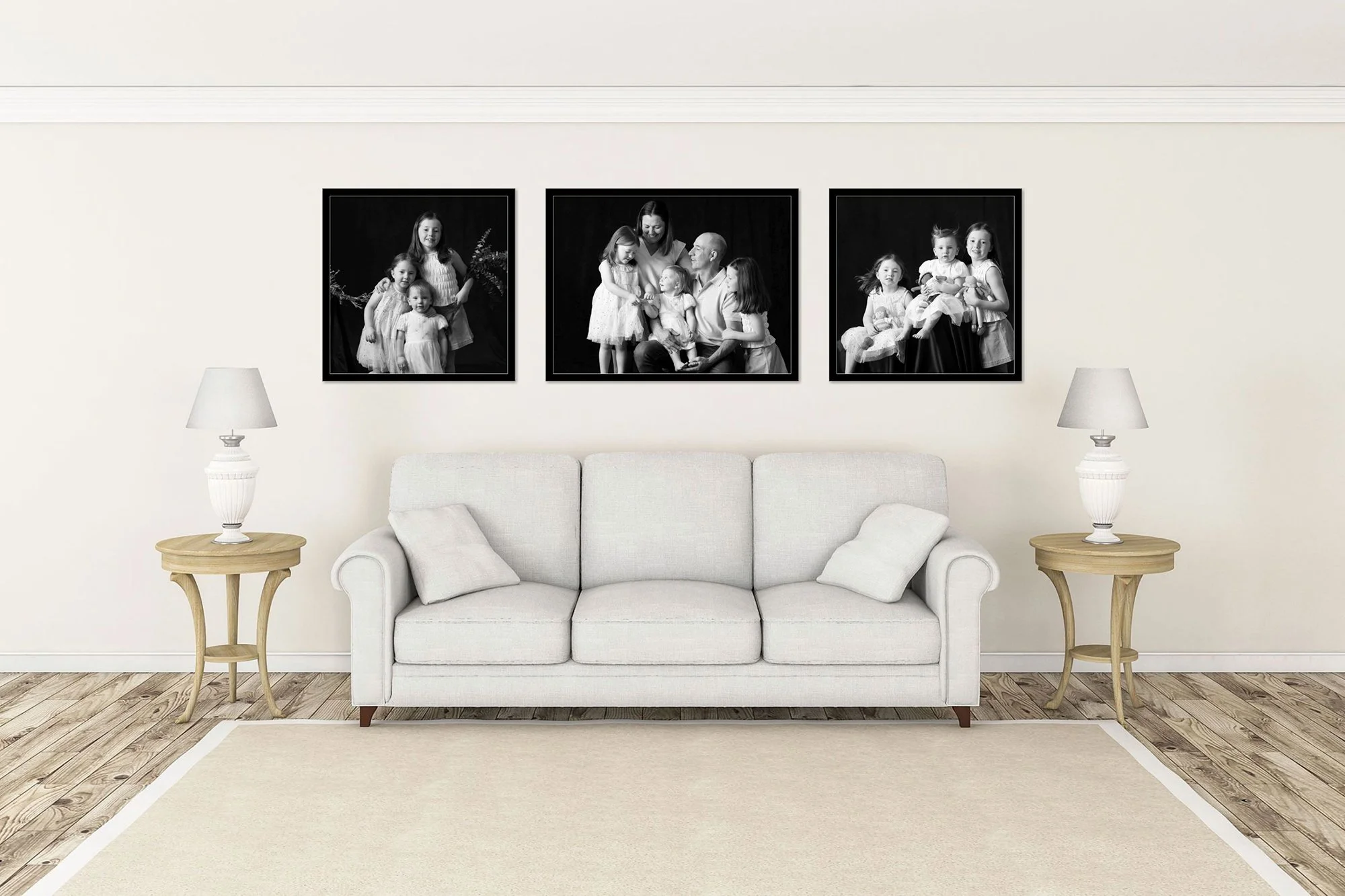 White sofa with two small pillows in front of a wall with three black-and-white family portraits, flanked by two side tables with lamps, in a living room with wooden flooring and beige rug.