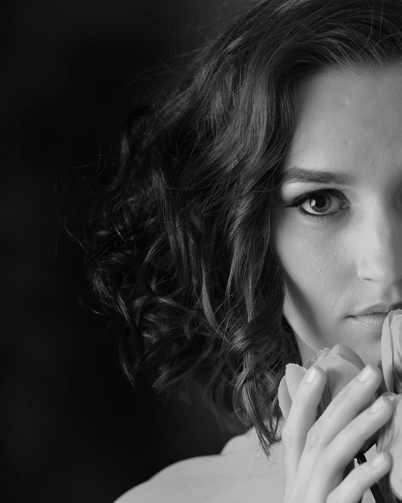 Black and white close-up of a woman's face with curly hair, holding a flower near her lips.