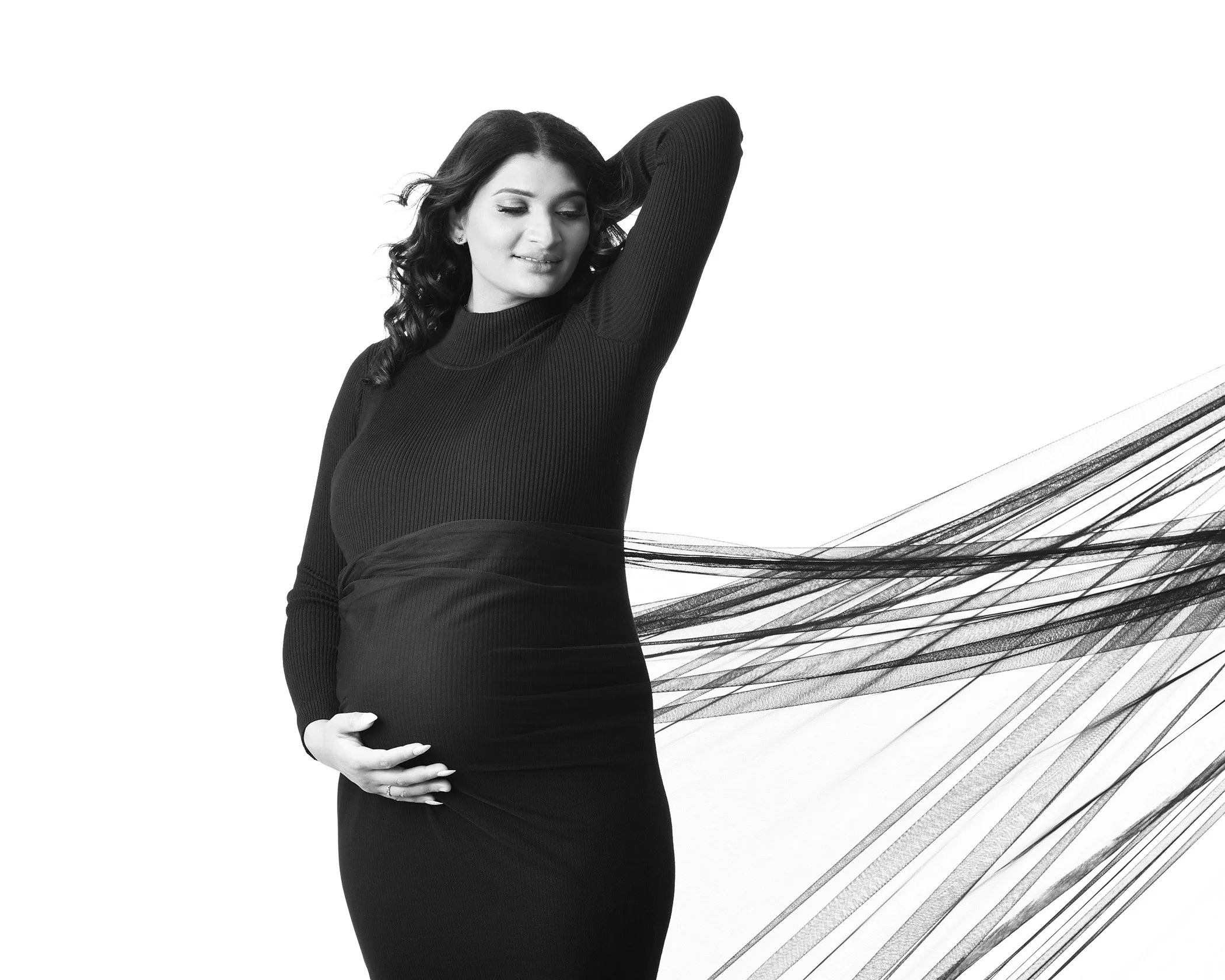 A pregnant woman in a black long-sleeve top gently holding her pregnant belly, standing against a white background with artistic black and white lines radiating from her waist.