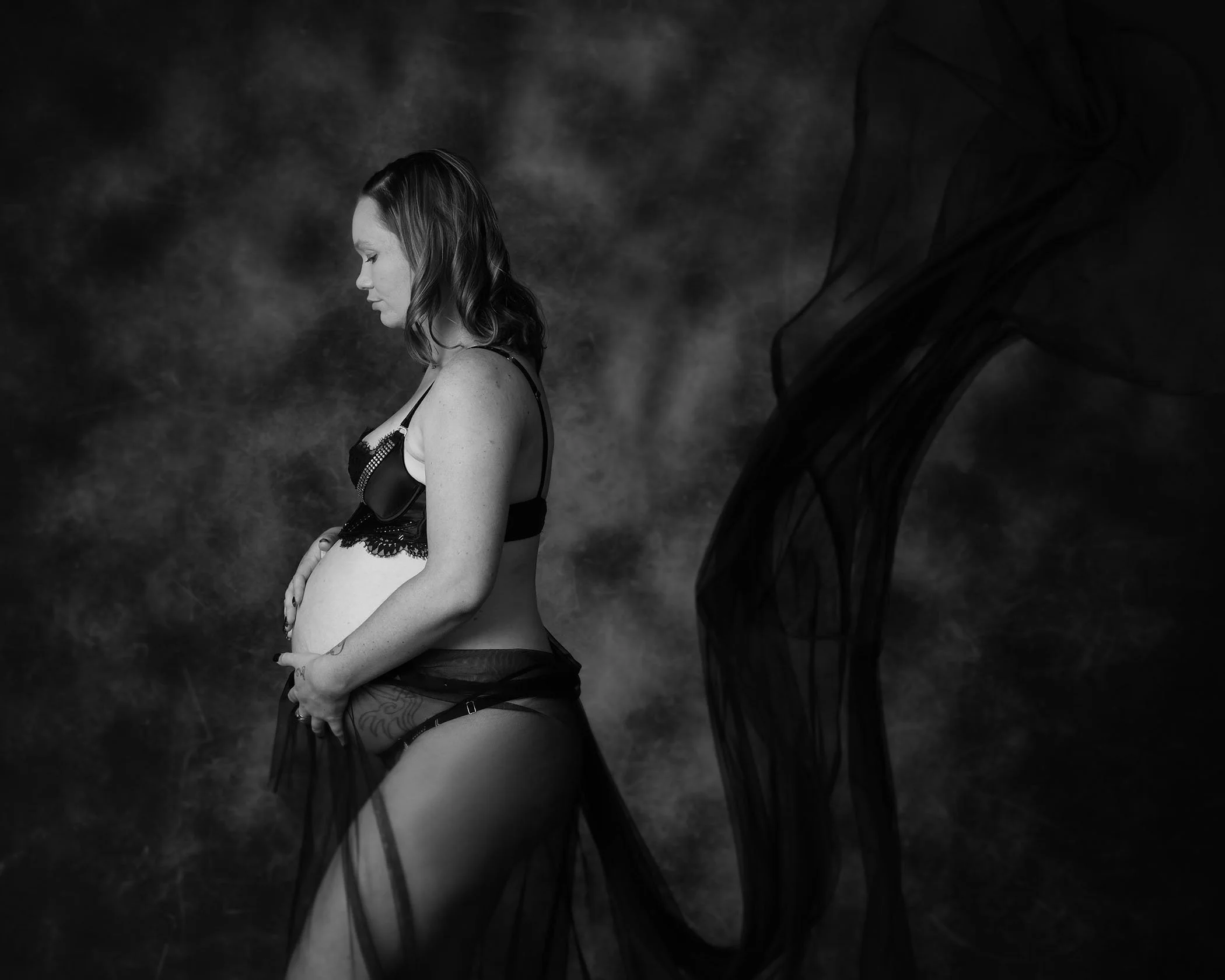 A woman with shoulder-length hair in lingerie, looking to the left, against a dark, smoky background with abstract shapes.