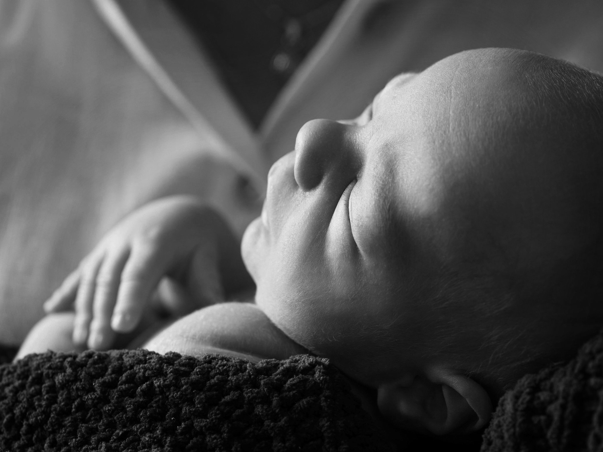Close-up black and white photo of a newborn baby lying on a blanket, sucking its thumb.