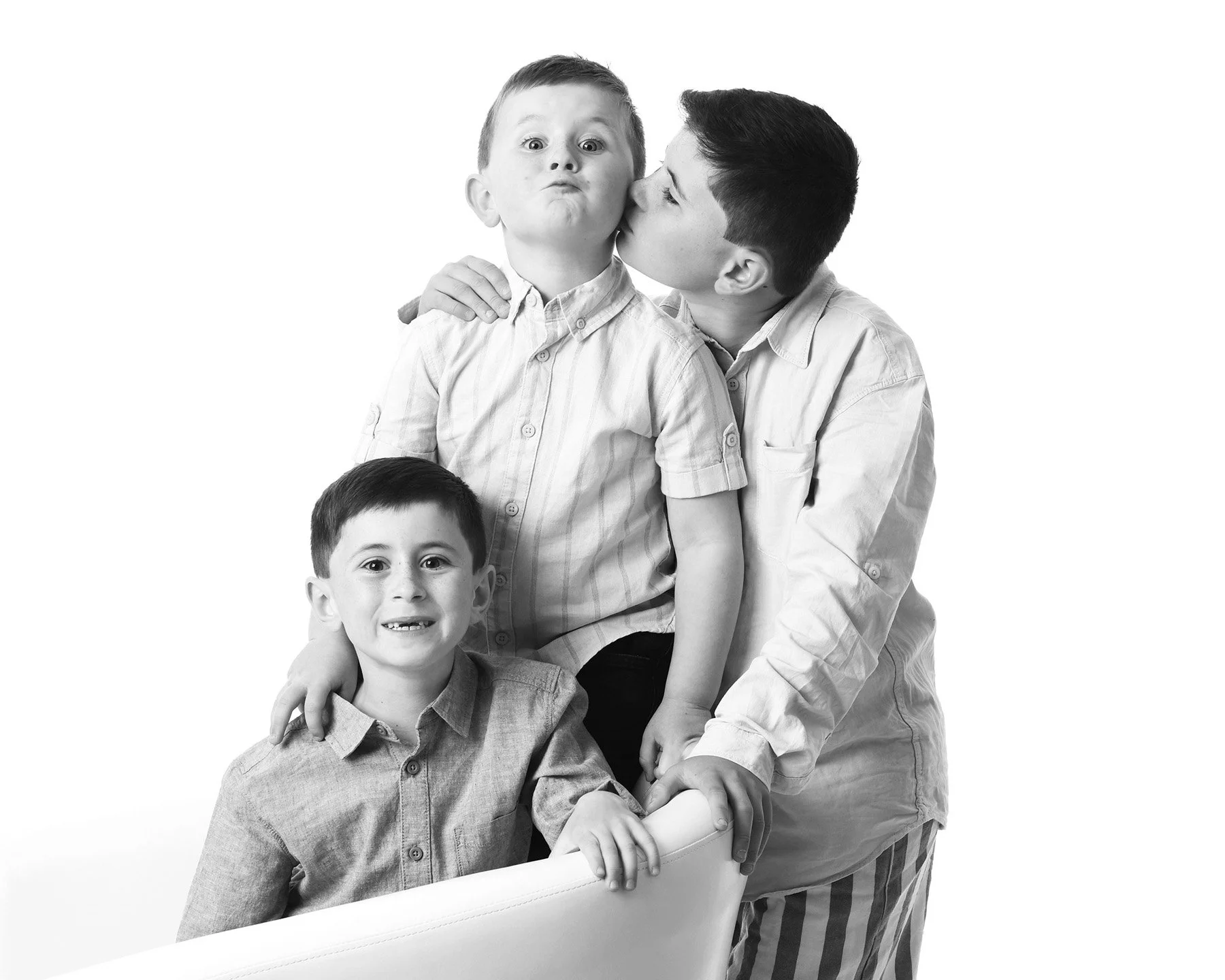 Black and white photo of four boys, with three boys visible, one with a surprised expression, another smiling, and the third being kissed on the cheek by the boy on the right.