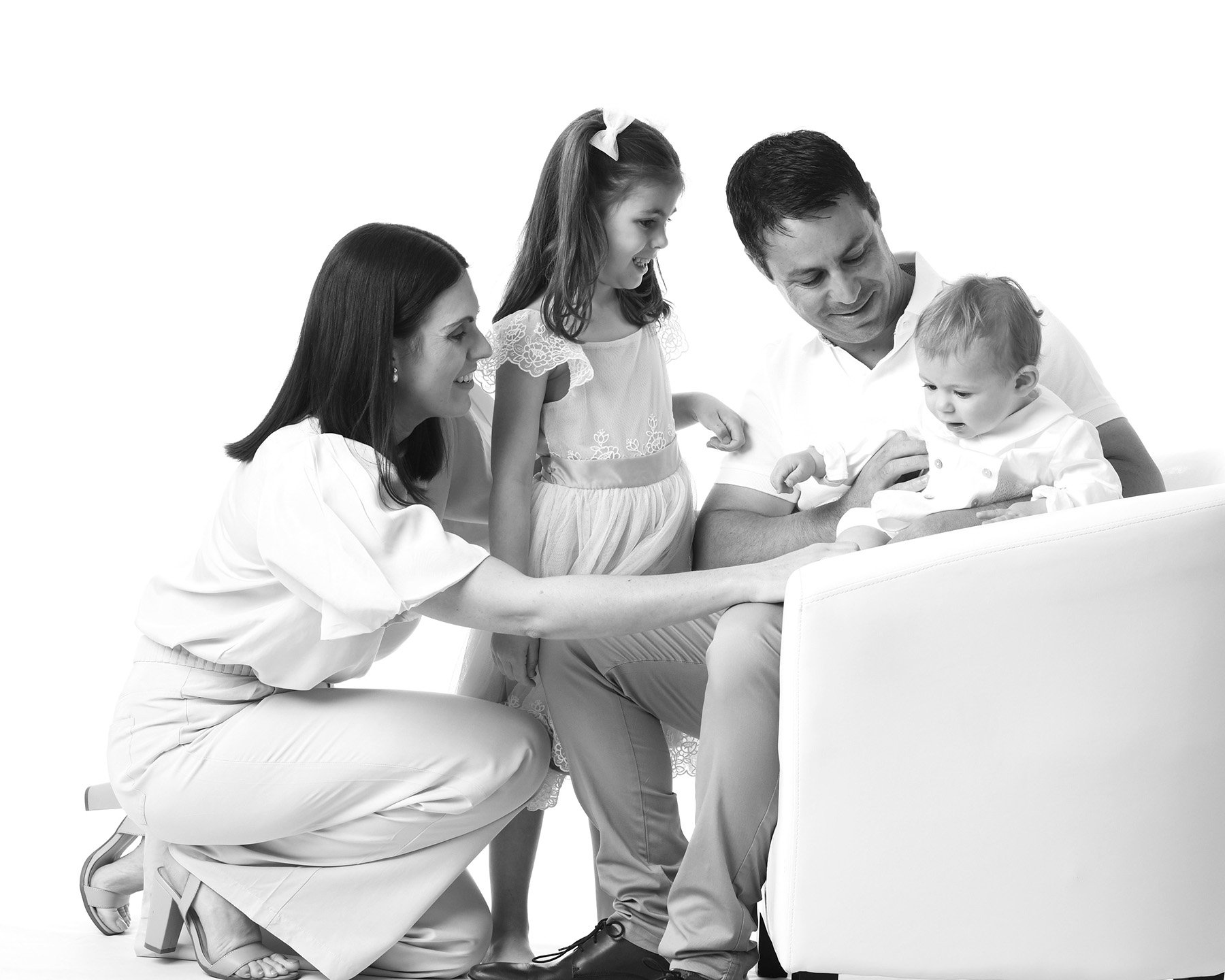 A family of four, including a mother, father, daughter, and baby, gathered around a laptop, smiling and engaging with the screen in a bright, white setting.
