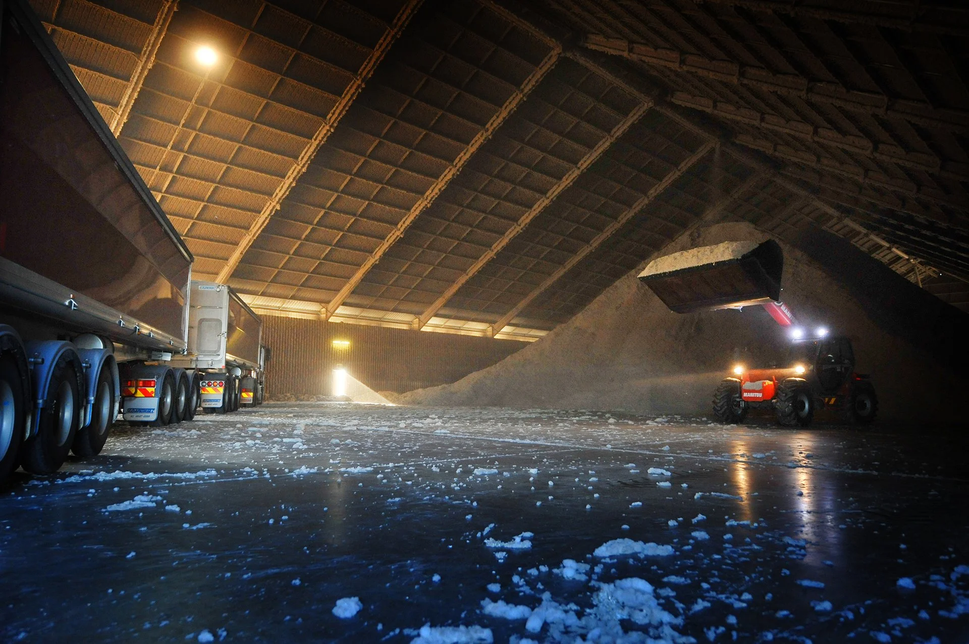 Indoor storage of snow removal equipment and vehicles, including a large truck, snowblower, and piles of snow with an arched roof ceiling