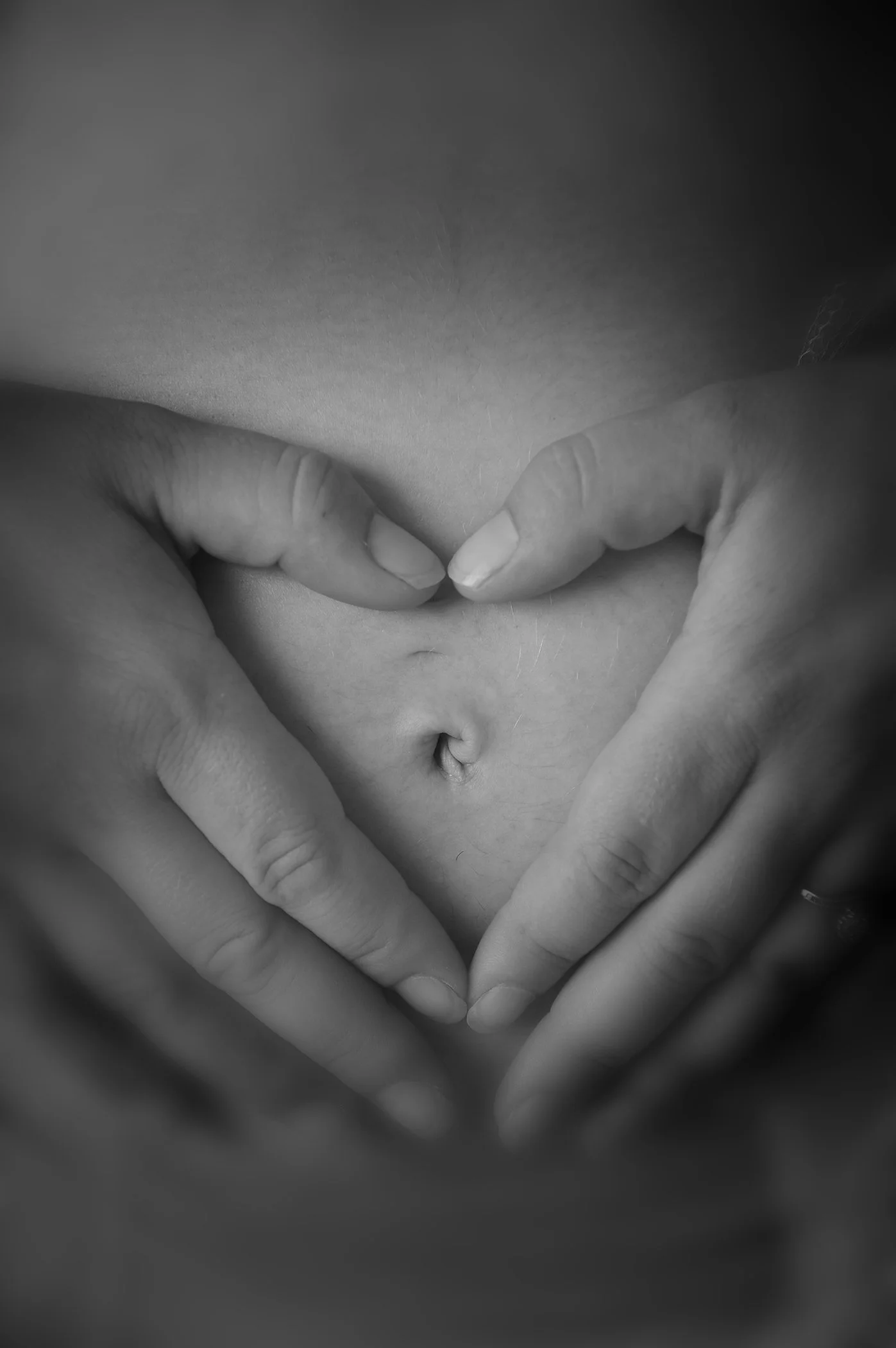 Black and white photo of a person making a heart shape with their hands over their stomach, with the fingers touching to form the top of the heart and the thumbs meeting at the bottom.