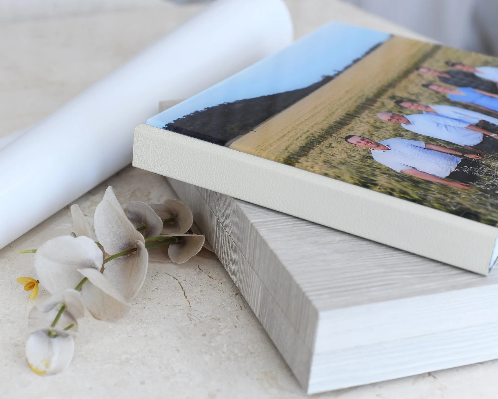 Close-up of a photo album with a group picture and white orchid flowers on a light-colored surface.