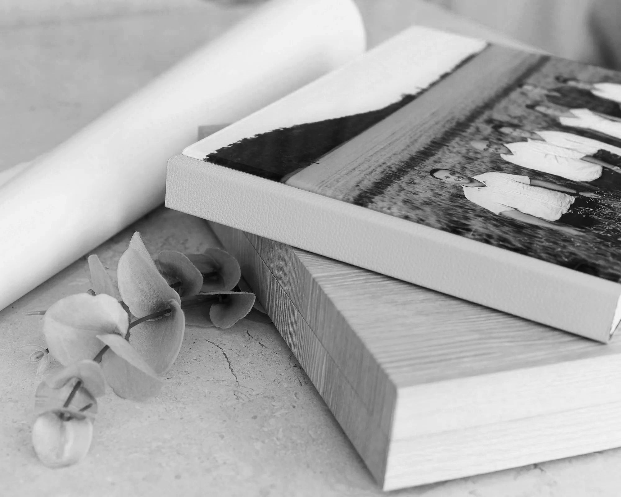 Close-up of a photo album with black-and-white photos, a white textured cover, and dried flowers on the side, all in a minimalistic black-and-white style.